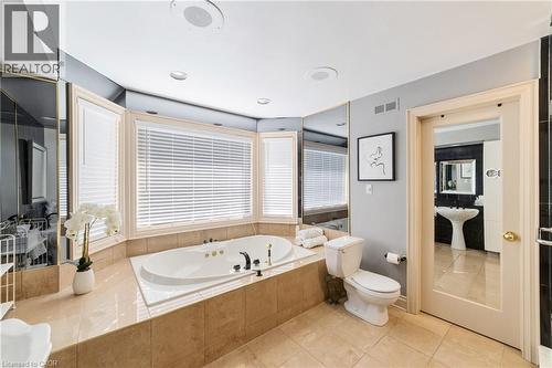 Bathroom featuring a built-in soaking tub with a tiled surround, bay windows with horizontal blinds, neutral floor tiling, and wall-mounted mirrors - 7775 St. Augustine Crescent, Niagara Falls, ON 