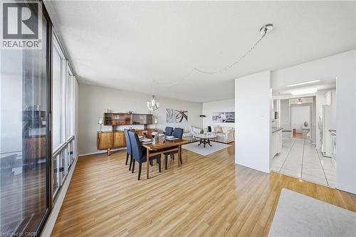 Open-concept living space featuring wood-finish flooring, a wall of windows, and a dedicated dining area with an overhead chandelier - 2055 Upper Middle Road Unit# 602, Burlington, ON 