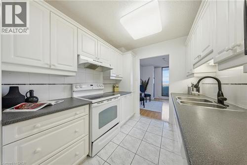 Galley kitchen featuring white cabinetry, gray countertops, a white tile backsplash, a double basin sink with a black faucet, and tiled flooring - 2055 Upper Middle Road Unit# 602, Burlington, ON 