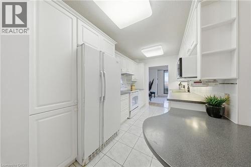 Bright kitchen featuring extensive white cabinetry, white appliances, tiled flooring, and a curved countertop with integrated sink - 2055 Upper Middle Road Unit# 602, Burlington, ON 