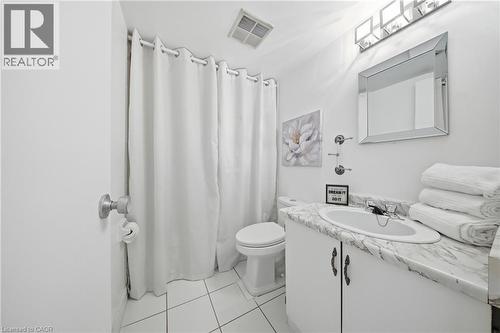 White tiled bathroom featuring a vanity with a white countertop, an undermount sink, and a framed mirror - 2055 Upper Middle Road Unit# 602, Burlington, ON 