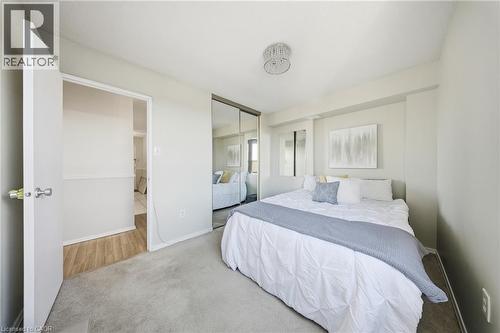 Carpeted sleeping area featuring a mirrored closet, a crystal chandelier, and a recessed wall niche - 2055 Upper Middle Road Unit# 602, Burlington, ON 