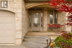 Stone facade entryway with concrete steps, a leaded glass front door with sidelights, and an arched garage door - 