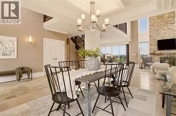 Open-concept living area featuring a multi-light chandelier, a stone-clad wall with a fireplace, expansive window walls, and a visible upper-level balcony - 