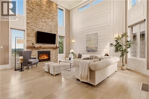 Living room featuring a floor-to-ceiling stone fireplace, soaring ceilings, extensive wainscoting, large windows, and light wood-finish flooring - 15 Mcwilliams Court, Cambridge, ON - Indoor Photo Showing Living Room With Fireplace