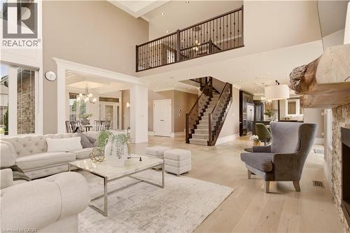 Grand living area featuring a double-height ceiling, light wood-finish flooring, a stone-clad fireplace with a substantial wood mantel, a prominent staircase with dark wood railings, and an upper-leve - 15 Mcwilliams Court, Cambridge, ON - Indoor Photo Showing Living Room With Fireplace