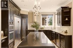 Gourmet kitchen featuring dark wood cabinetry, a large center island with a dark countertop, stainless steel appliances, and light-colored subway tile backsplash - 