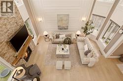 Expansive living area featuring a floor-to-ceiling stone fireplace, natural wood mantel, two-story windows, light wood-finish flooring, and decorative wall paneling - 