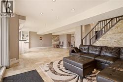 Spacious living area featuring large format tile flooring, a stone-clad accent wall, and a staircase with dark wood-finish handrails and black metal balusters - 