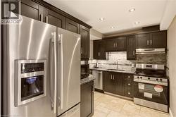Kitchen featuring dark wood cabinetry, stainless steel appliances, stone countertops, a mosaic tile backsplash, and light-toned tile flooring - 