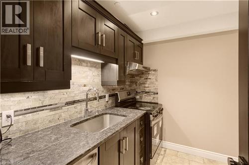 Compact kitchen featuring dark wood cabinetry, stainless steel appliances, granite countertops, and a stacked stone backsplash - 15 Mcwilliams Court, Cambridge, ON - Indoor Photo Showing Kitchen