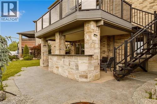 Expansive stamped concrete patio featuring a stone-clad outdoor bar and an overhead deck with glass panel railings - 15 Mcwilliams Court, Cambridge, ON - Outdoor