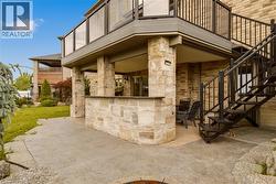 Expansive stamped concrete patio featuring a stone-clad outdoor bar and an overhead deck with glass panel railings - 