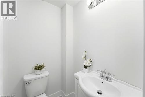 White toilet with a chrome flush lever, a white porcelain pedestal sink, chrome two-handle faucet, and a chrome vanity light fixture - 968 Main Street E, Hamilton, ON 
