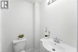 White toilet with a chrome flush lever, a white porcelain pedestal sink, chrome two-handle faucet, and a chrome vanity light fixture - 
