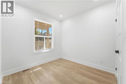 Room featuring light wood-finish flooring, white painted walls, and a single window with horizontal blinds - 968 Main Street E, Hamilton, ON 