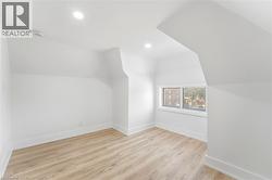 Attic room featuring wood-finish flooring, white walls, recessed ceiling lighting, and a single window - 