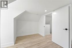 Finished attic space featuring light wood-finish flooring, crisp white walls, recessed lighting, and a modern slab door with matte black hardware - 