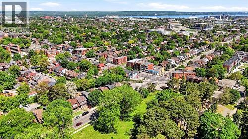 Expansive aerial view showcasing a verdant neighborhood with a mix of residential structures and multi-story buildings, abundant mature trees, a visible body of water in the distance, and an athletic - 968 Main Street E, Hamilton, ON 