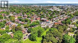 Expansive aerial view showcasing a verdant neighborhood with a mix of residential structures and multi-story buildings, abundant mature trees, a visible body of water in the distance, and an athletic - 