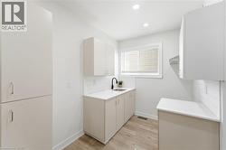 Utility room featuring light wood-finish flooring, white cabinetry, a single basin sink with a matte black faucet, and white subway tile backsplash - 