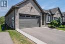 Stone facade residence featuring a two-car garage with dark gray paneling, an asphalt driveway, concrete sidewalks, and an arched window with louvered blinds - 15 Winterberry Lane, Waterford, ON 