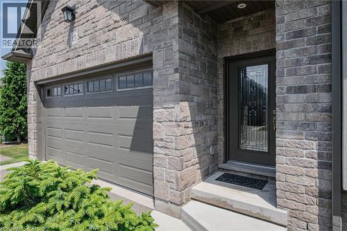 Stone facade with integrated garage featuring upper window panels, concrete steps, and a decorative glass entry door - 15 Winterberry Lane, Waterford, ON 