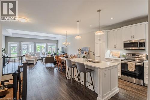 Open-concept living space featuring wood-finish flooring, a contemporary kitchen island with seating, white shaker cabinetry, stainless steel appliances, and abundant natural light from multiple windo - 15 Winterberry Lane, Waterford, ON 
