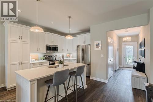 Kitchen featuring white cabinetry, stainless steel appliances, a center island with sink, pendant lighting, and wood-finish flooring - 15 Winterberry Lane, Waterford, ON 