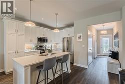 Kitchen featuring white cabinetry, stainless steel appliances, a center island with sink, pendant lighting, and wood-finish flooring - 