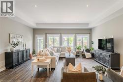 Spacious living area featuring wood-finish flooring, a tray ceiling with recessed lighting, and a wall of windows and an exterior door providing ample natural light - 