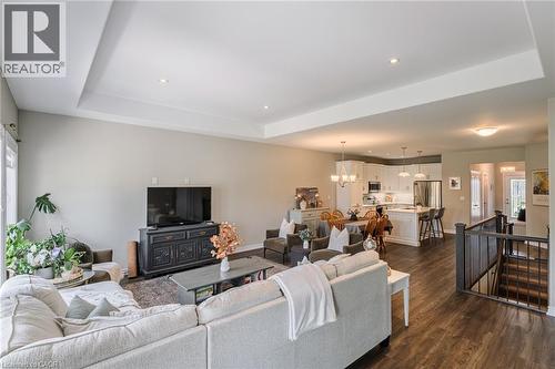 Open-concept living area featuring tray ceilings with recessed lighting, wood-finish flooring, and a kitchen with white cabinetry and stainless steel appliances - 15 Winterberry Lane, Waterford, ON 