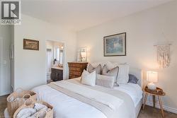 Spacious bedroom featuring light-toned walls, neutral carpeting, and a doorway to a bathroom with a dark wood-finish vanity and white countertop - 