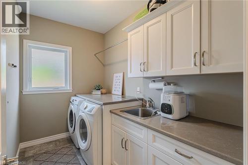 Functional laundry room featuring white cabinetry, a built-in sink, ample counter space, a frosted window, and a clothes hanging rod - 15 Winterberry Lane, Waterford, ON 
