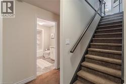 Carpeted staircase with dark handrail and balusters, featuring a doorway leading to a bathroom with a white vanity, toilet, and tub/shower combination - 