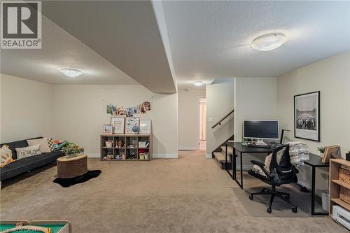 Expansive carpeted room featuring a built-in staircase with dark wood handrail, light beige walls, and flush-mount ceiling lighting - 15 Winterberry Lane, Waterford, ON 