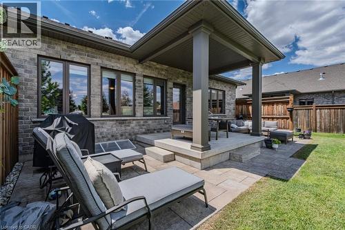 Expansive backyard featuring a manicured lawn, a large paver patio, a covered patio area with structural columns, and a brick exterior - 15 Winterberry Lane, Waterford, ON 