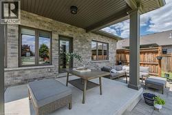 Covered outdoor patio featuring a brick exterior, concrete flooring, and a wood privacy fence - 
