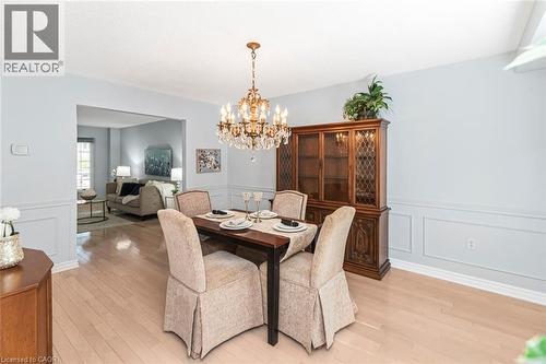 Dining area featuring wood-finish flooring, wainscoting, and an ornate crystal chandelier - 85 Citation Crescent, Ancaster, ON 