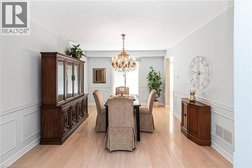 Dining area featuring light wood-finish flooring, wainscoting, a crystal chandelier, and ample natural light from a window - 85 Citation Crescent, Ancaster, ON 