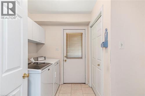 Laundry area featuring white cabinetry, a built-in washing machine and dryer, and tiled flooring - 85 Citation Crescent, Ancaster, ON 