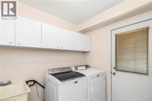 Laundry area featuring white upper cabinetry, a utility sink with dual faucets, and a white door with horizontal blinds - 85 Citation Crescent, Ancaster, ON 