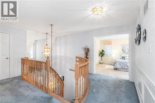 Upper-level hallway featuring a curved wood banister with traditional balusters, plush blue carpeting, and a decorative pendant light fixture - 85 Citation Crescent, Ancaster, ON 