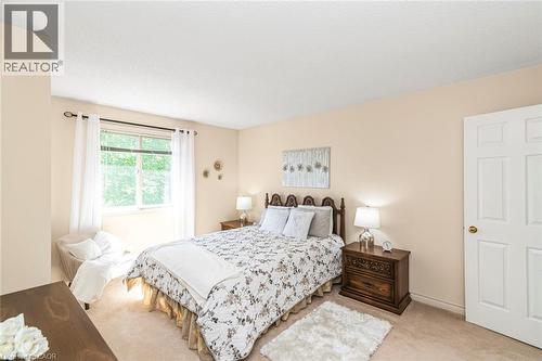 Bedroom featuring a large window with white sheer curtains, beige carpeting, light cream walls, and a white paneled door - 85 Citation Crescent, Ancaster, ON 