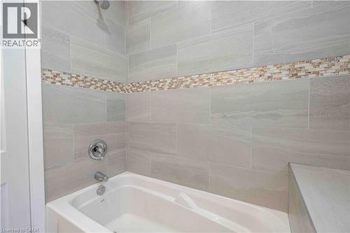 Bathtub and shower combination featuring large format grey wall tiles, a decorative mosaic tile accent band, and a chrome shower head and faucet - 204 Glow Avenue Unit# Upper, Hamilton, ON 
