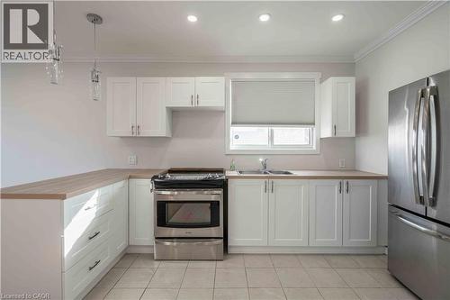 Kitchen featuring white shaker-style cabinetry, wood-finish countertops, stainless steel appliances, and tiled flooring - 204 Glow Avenue Unit# Upper, Hamilton, ON 