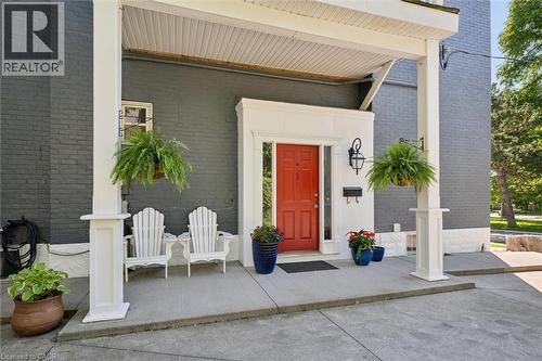 Covered porch entry featuring a vibrant red door, a black exterior lantern, and dark gray brick siding - 149 Young Street, Kitchener, ON - Outdoor