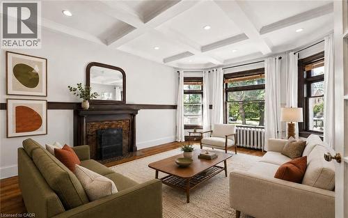 Living area featuring a coffered ceiling, a decorative fireplace with a dark wood mantel, hardwood flooring, and bay windows - 149 Young Street, Kitchener, ON - Indoor Photo Showing Living Room With Fireplace