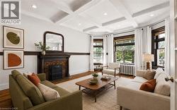 Living area featuring a coffered ceiling, a decorative fireplace with a dark wood mantel, hardwood flooring, and bay windows - 