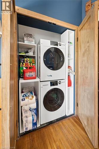 Stacked washer and dryer unit within a built-in closet, featuring natural wood doors and trim, white shelving, and wood-finish flooring - 149 Young Street, Kitchener, ON - Indoor Photo Showing Laundry Room